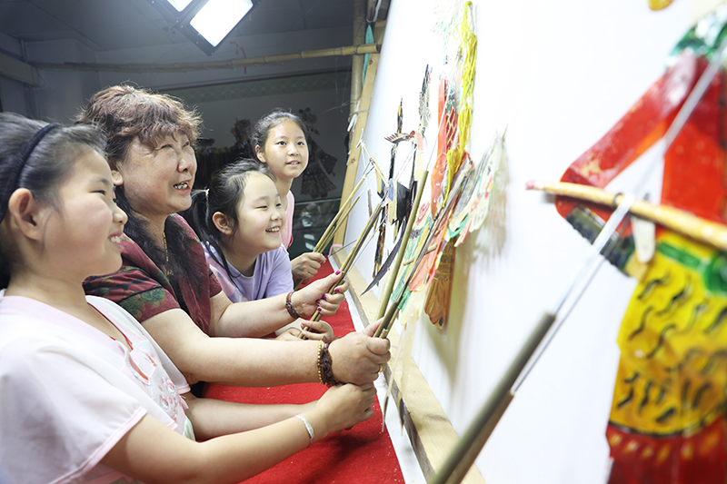 皮影藝人指導小朋友表演皮影戲。